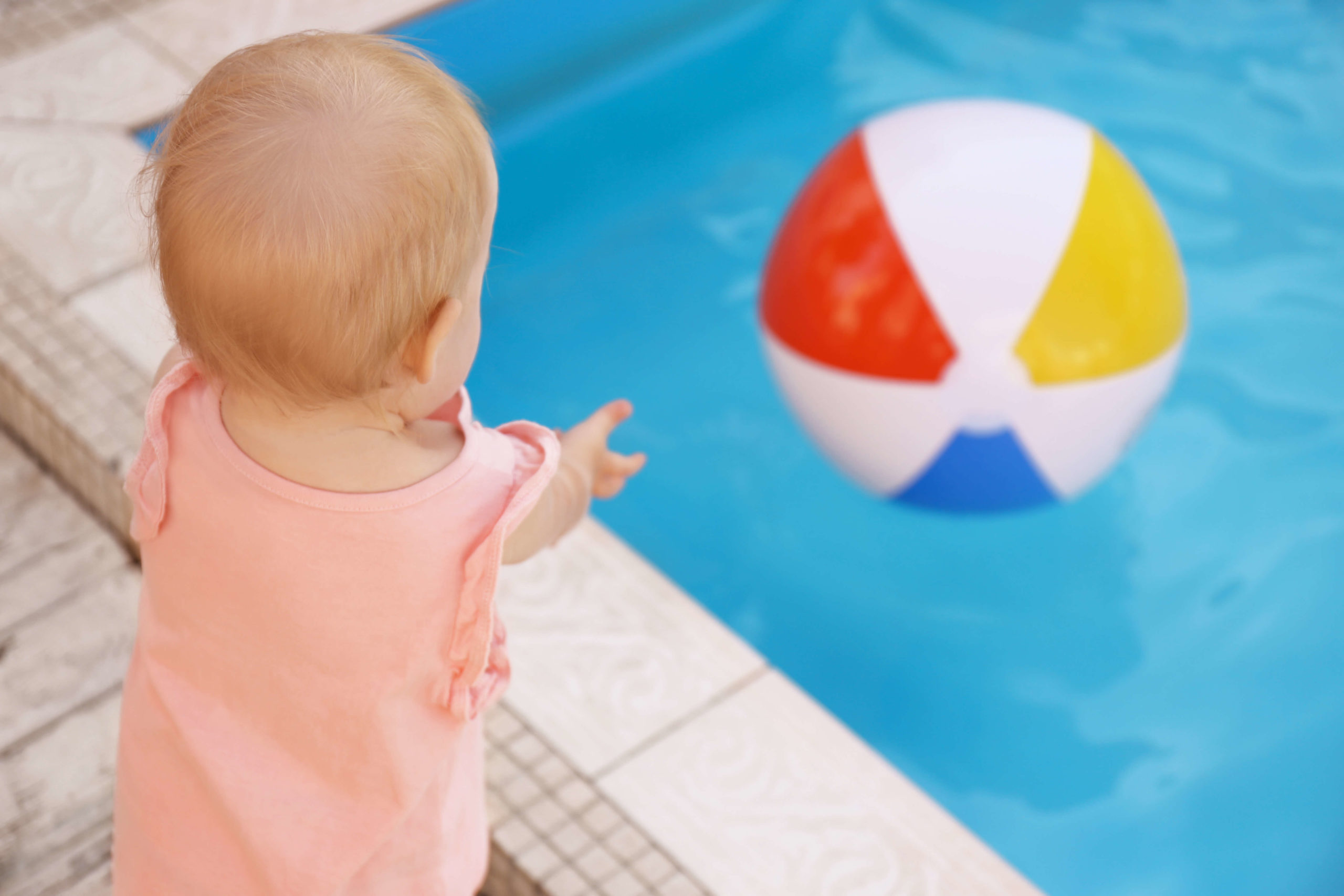 Pool safety and child reaching for beach ball in pool